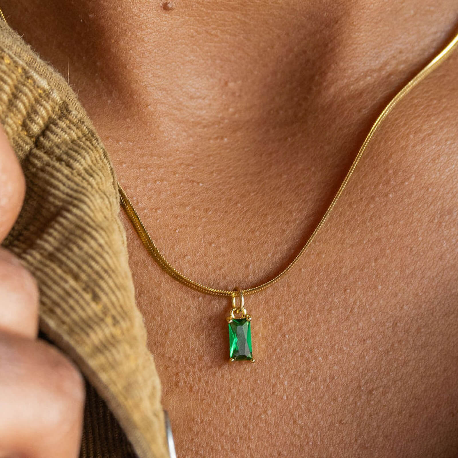 Gold necklace with a green pendant on a person's neck
