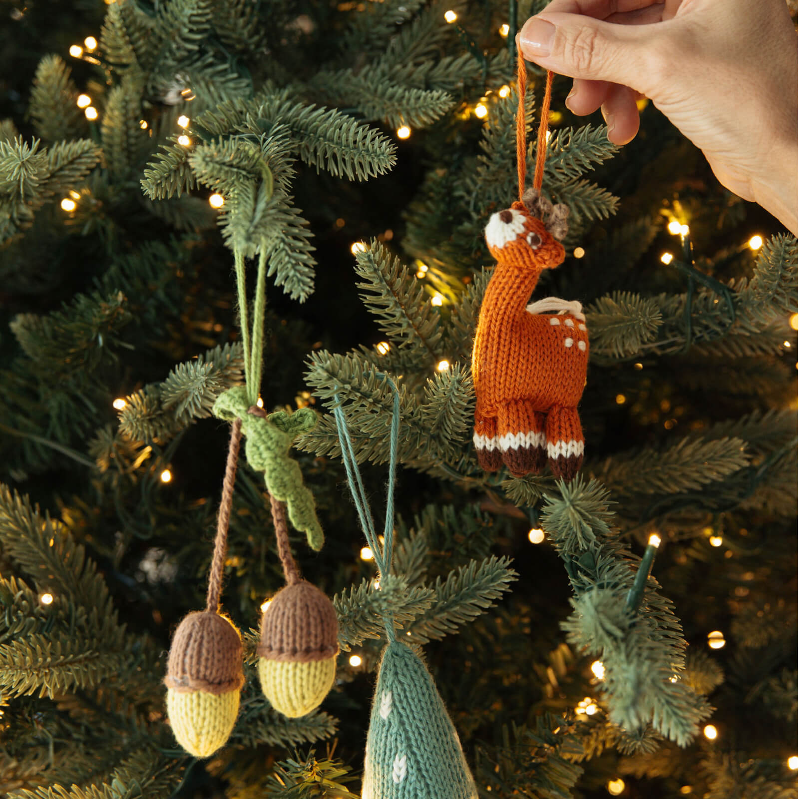 Handmade knitted ornaments on a Christmas tree with warm lighting.