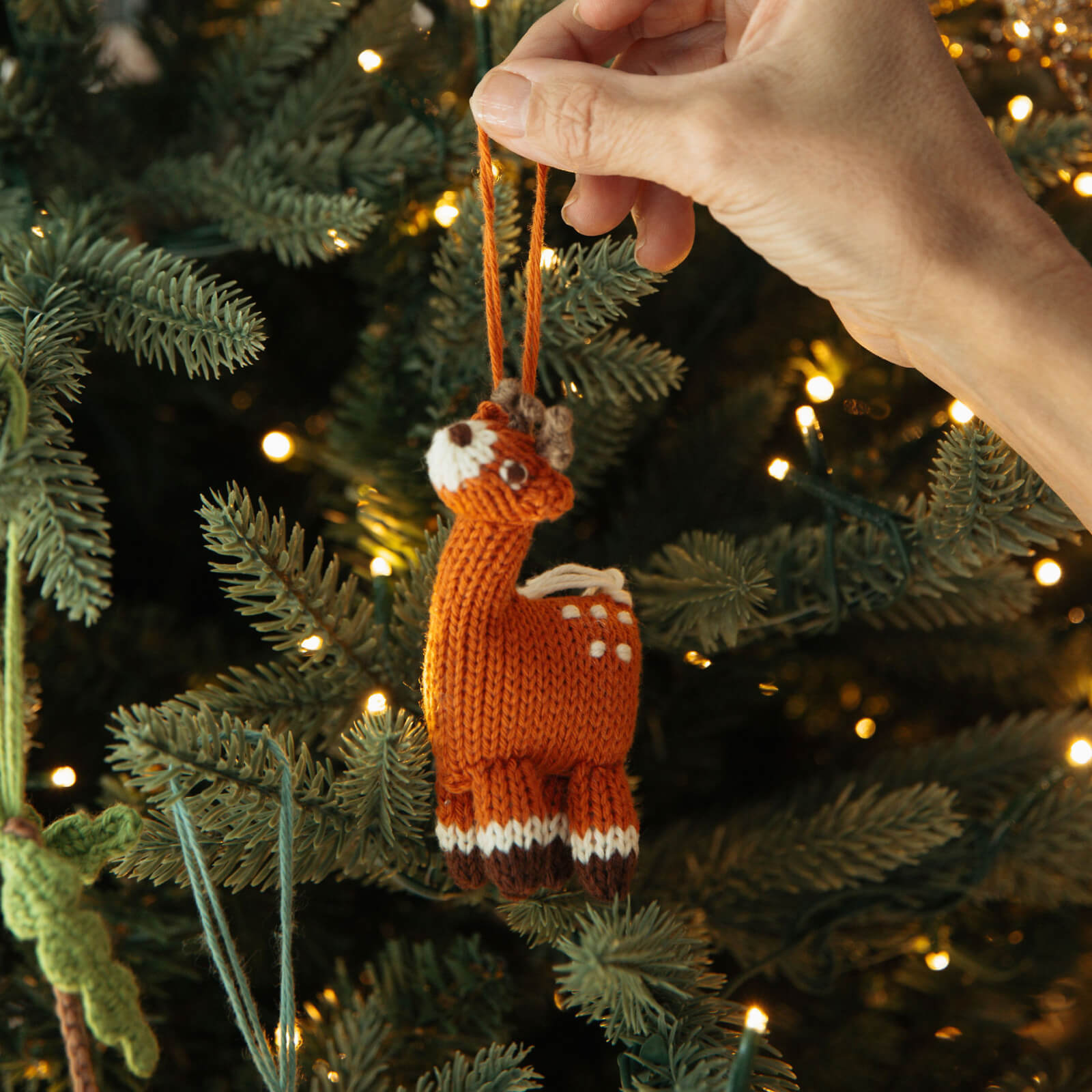 Hand holding a knitted deer ornament against a Christmas tree background