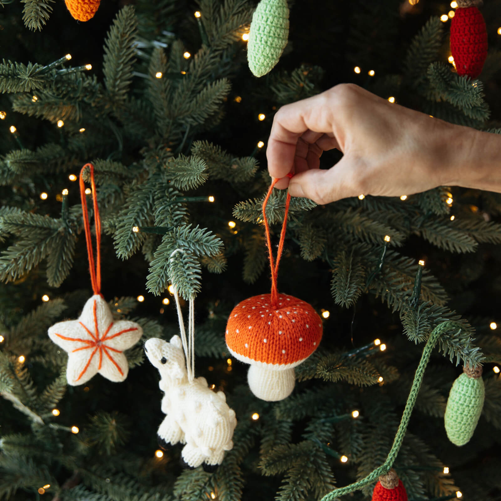 Hand selecting a knitted Christmas ornament from a decorated tree.