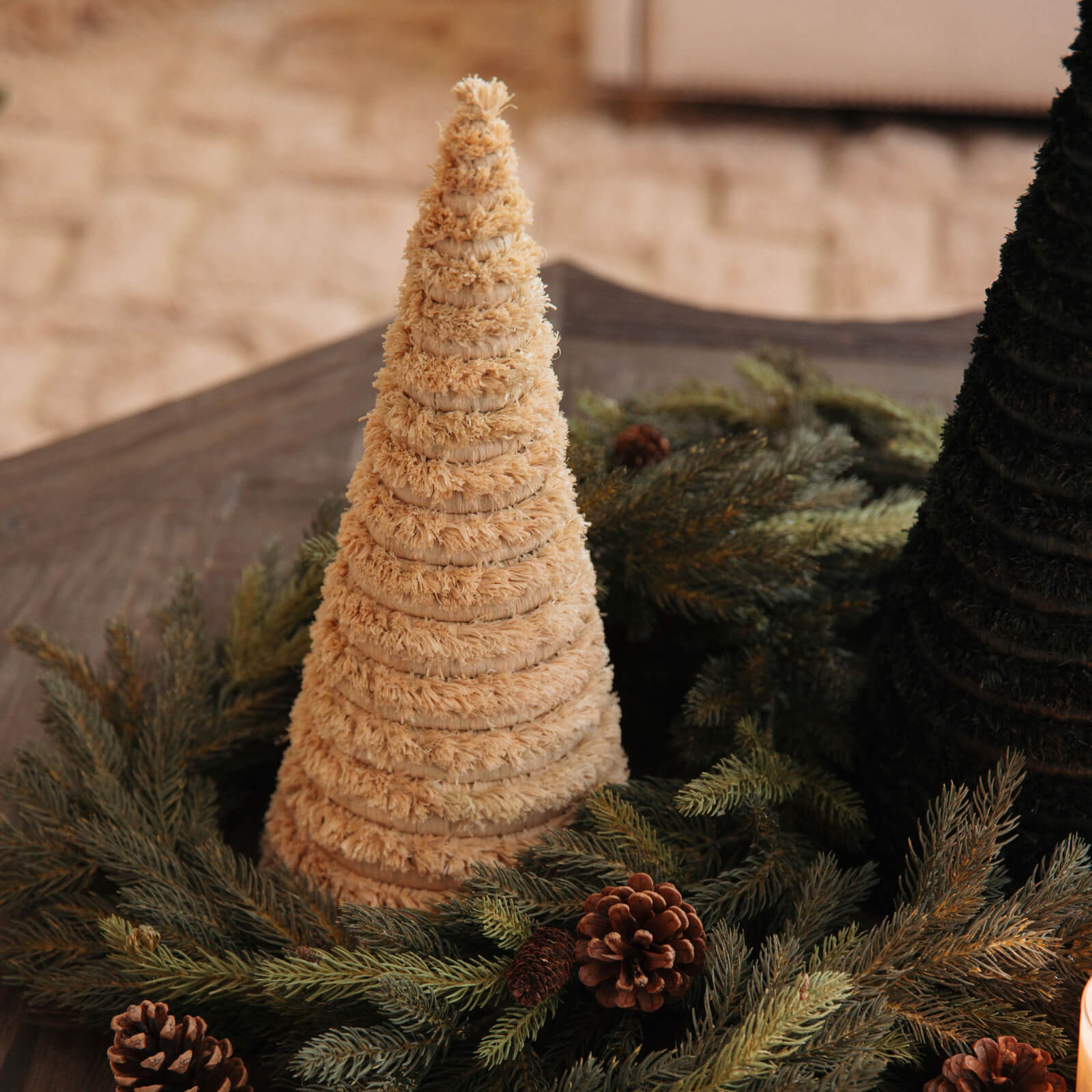 Textured cone-shaped Christmas tree on a bed of greenery with pine cones.