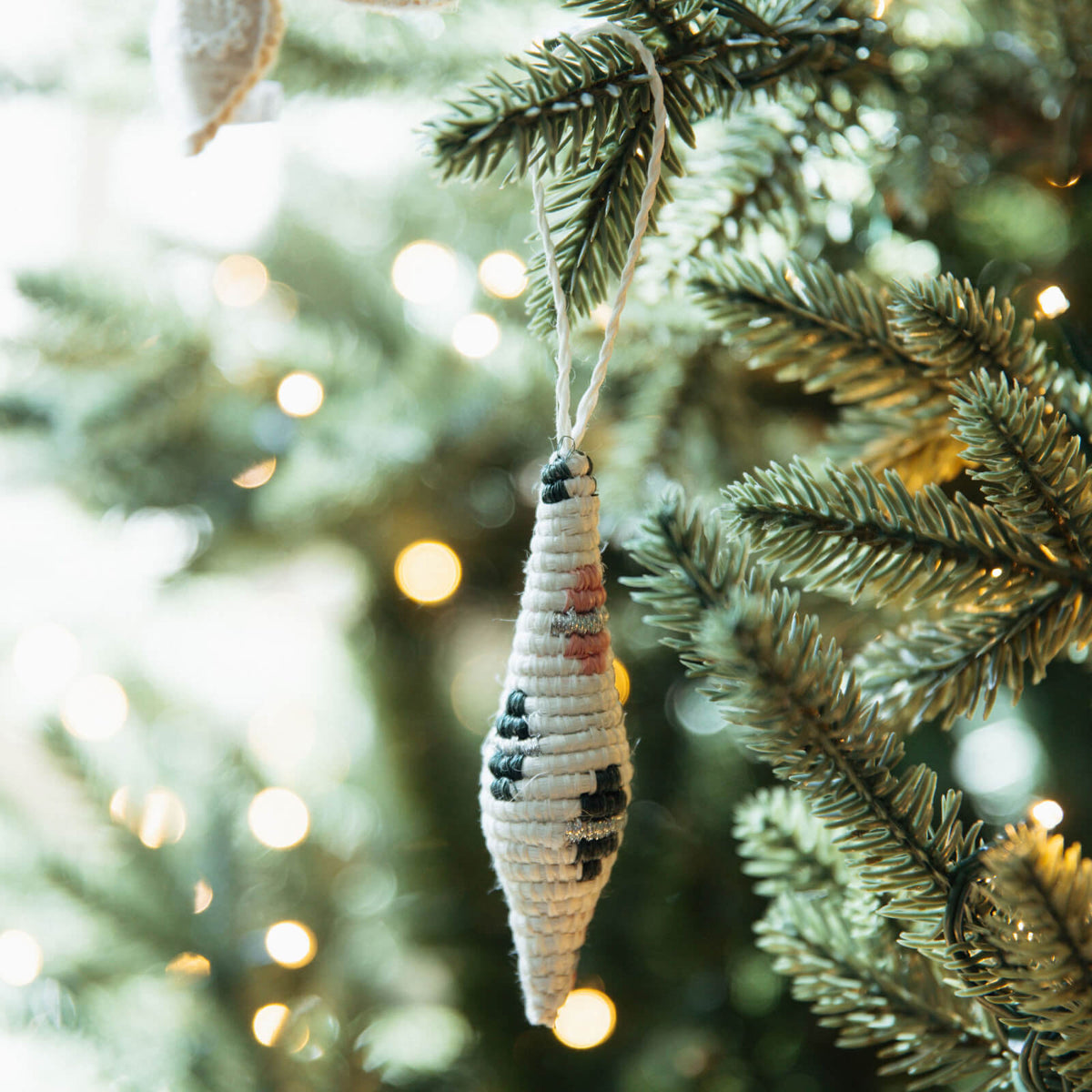 Decorative icicle ornament hanging on a Christmas tree with blurred lights in the background