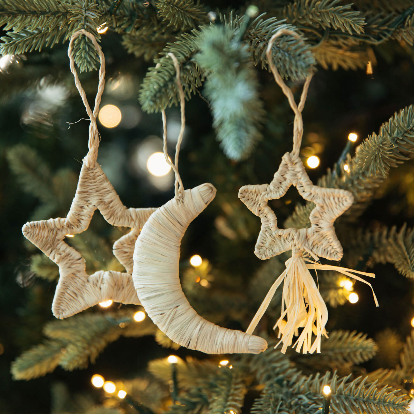 Decorative star and moon ornaments hanging on a Christmas tree with blurred lights in the background.