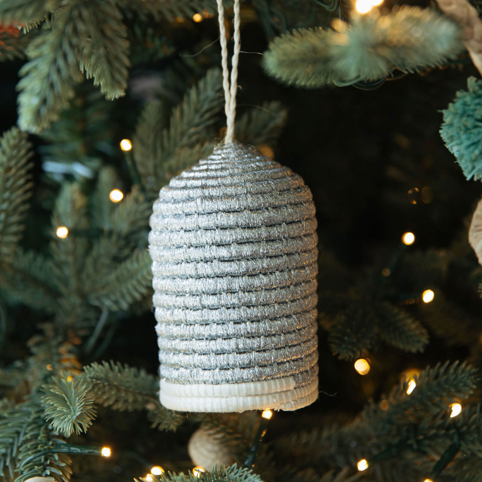 Textured silver bell ornament hanging on a Christmas tree with lights.