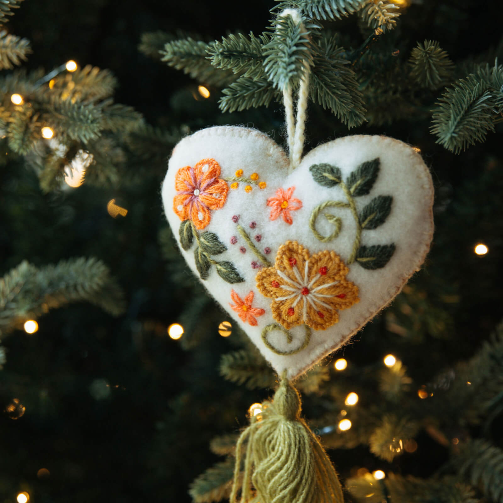 Decorative heart ornament with floral embroidery hanging on a Christmas tree.