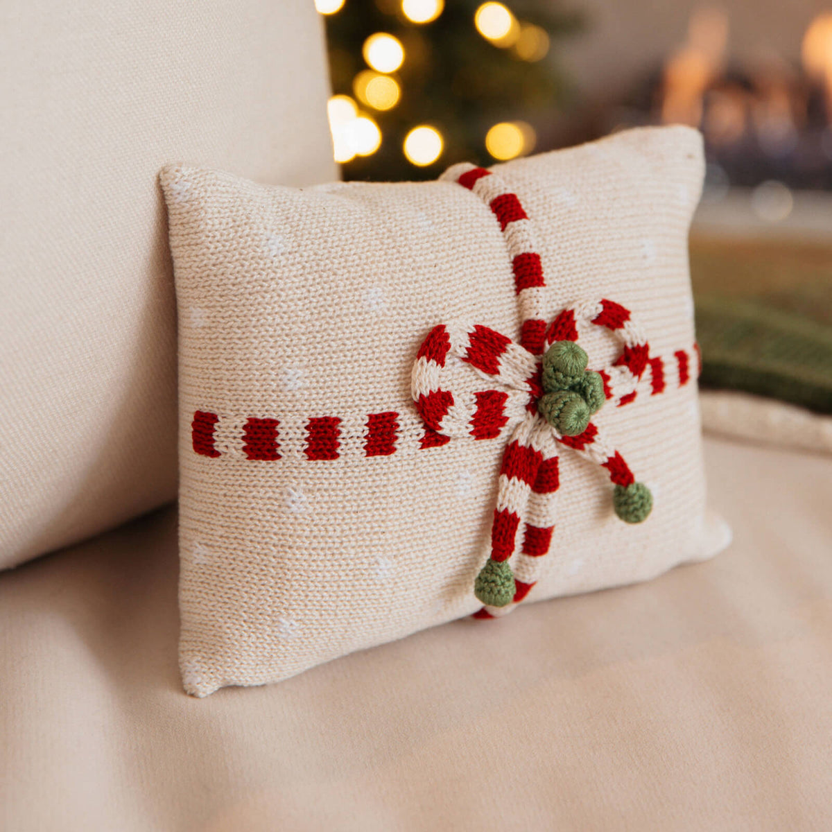 Decorative pillow with candy cane design on a couch with a blurred Christmas tree in the background