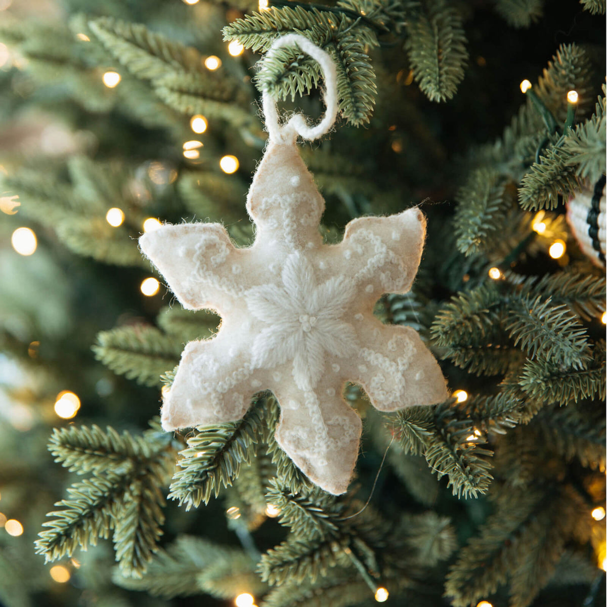 White snowflake ornament on a decorated Christmas tree with lights.