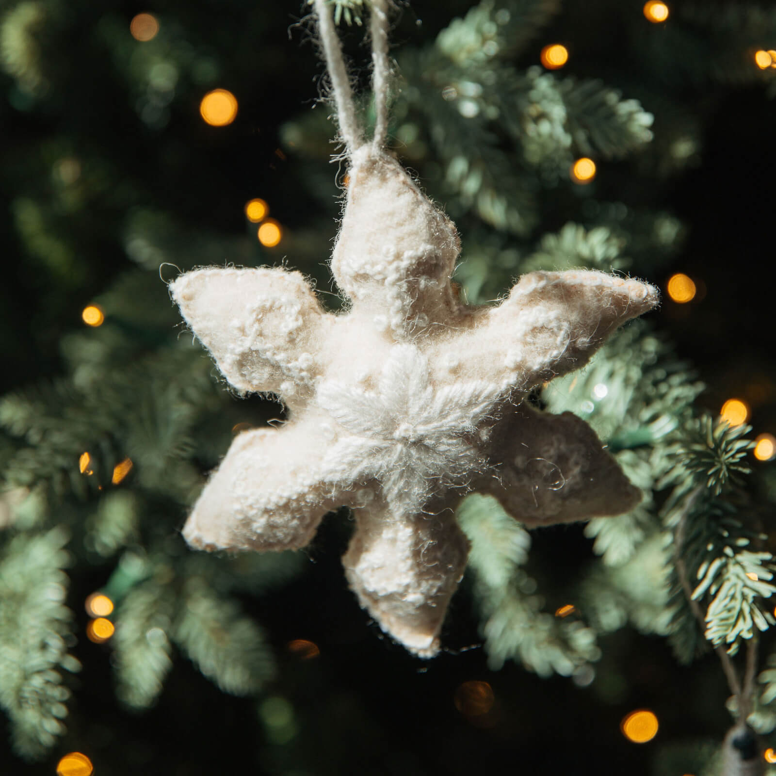 Textured star-shaped ornament hanging on a Christmas tree with blurred lights in the background