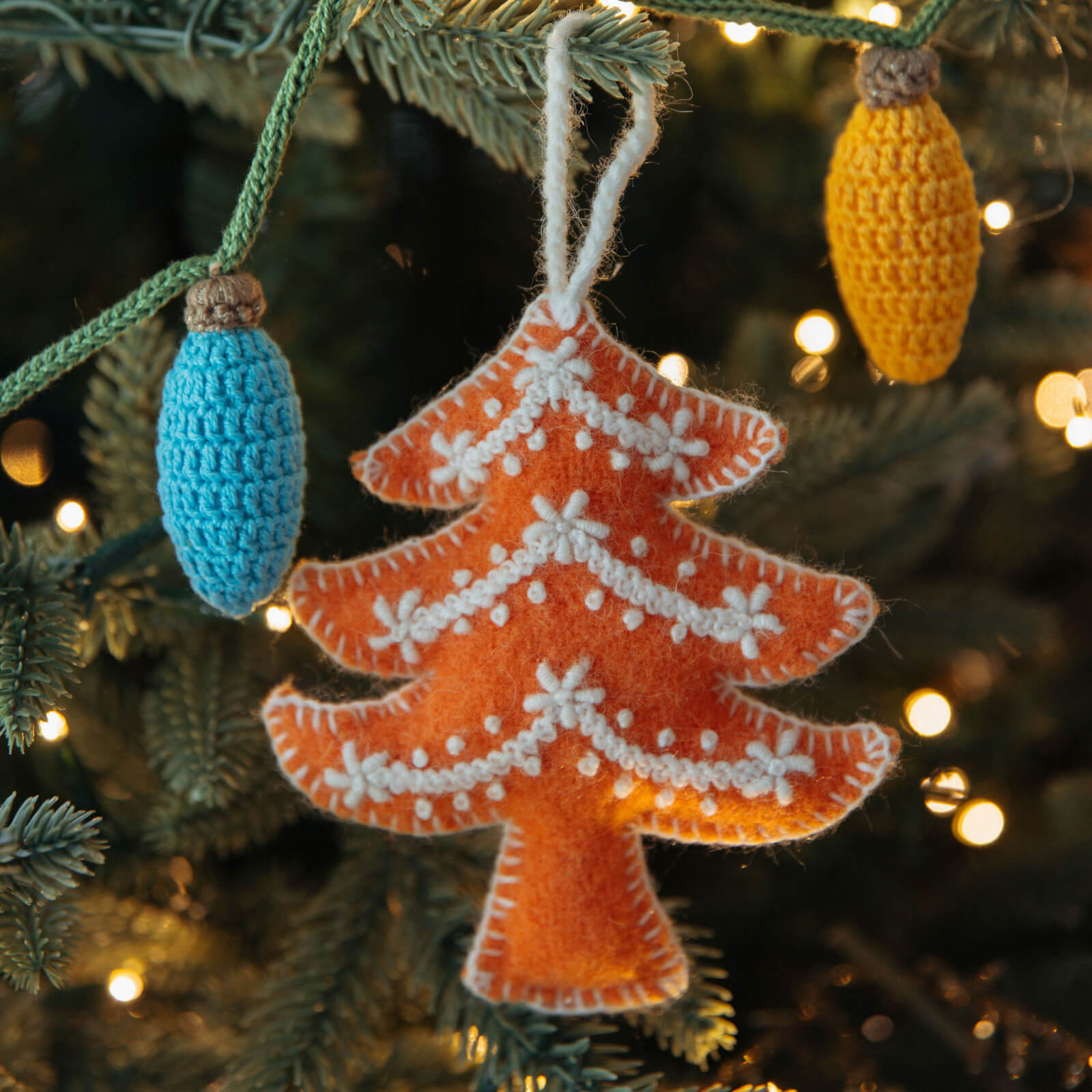 Handmade Christmas tree ornament on a decorated tree with lights in the background