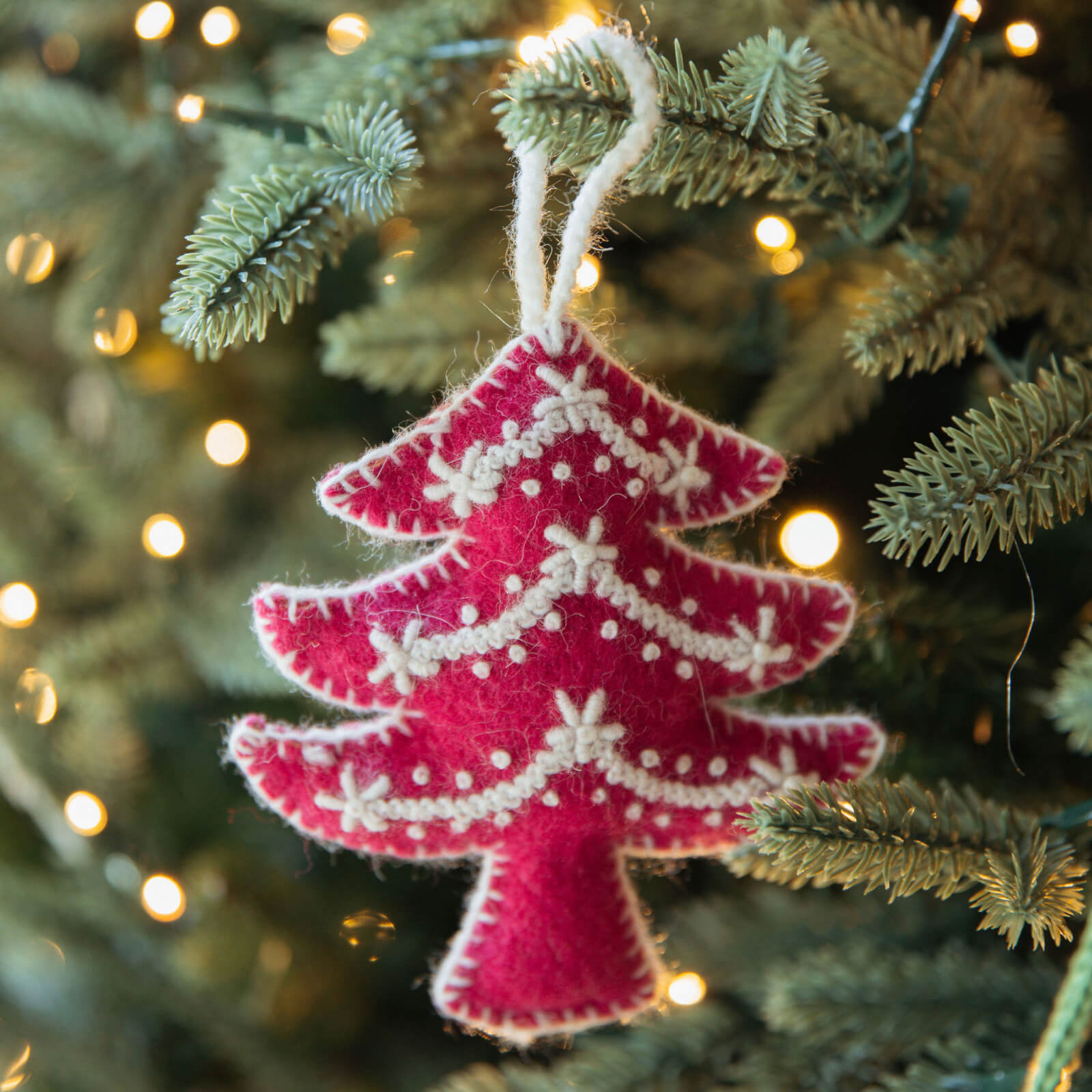Pink Christmas tree ornament hanging on a decorated tree with lights.