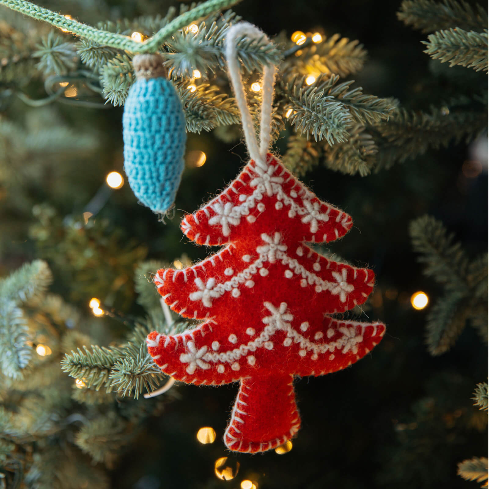 Red Christmas tree ornament with white snowflakes hanging on a decorated tree.