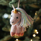 Knitted unicorn ornament hanging on a Christmas tree with blurred lights in the background