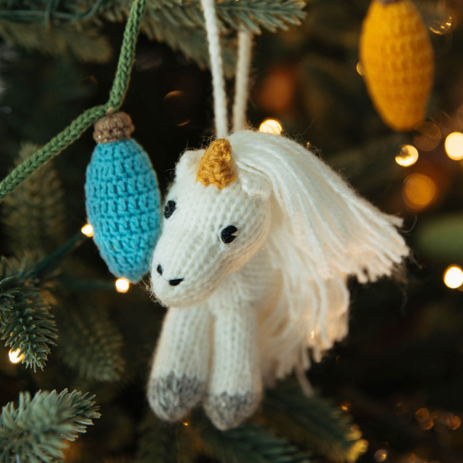 Knitted unicorn ornament hanging on a Christmas tree with blurred lights in the background