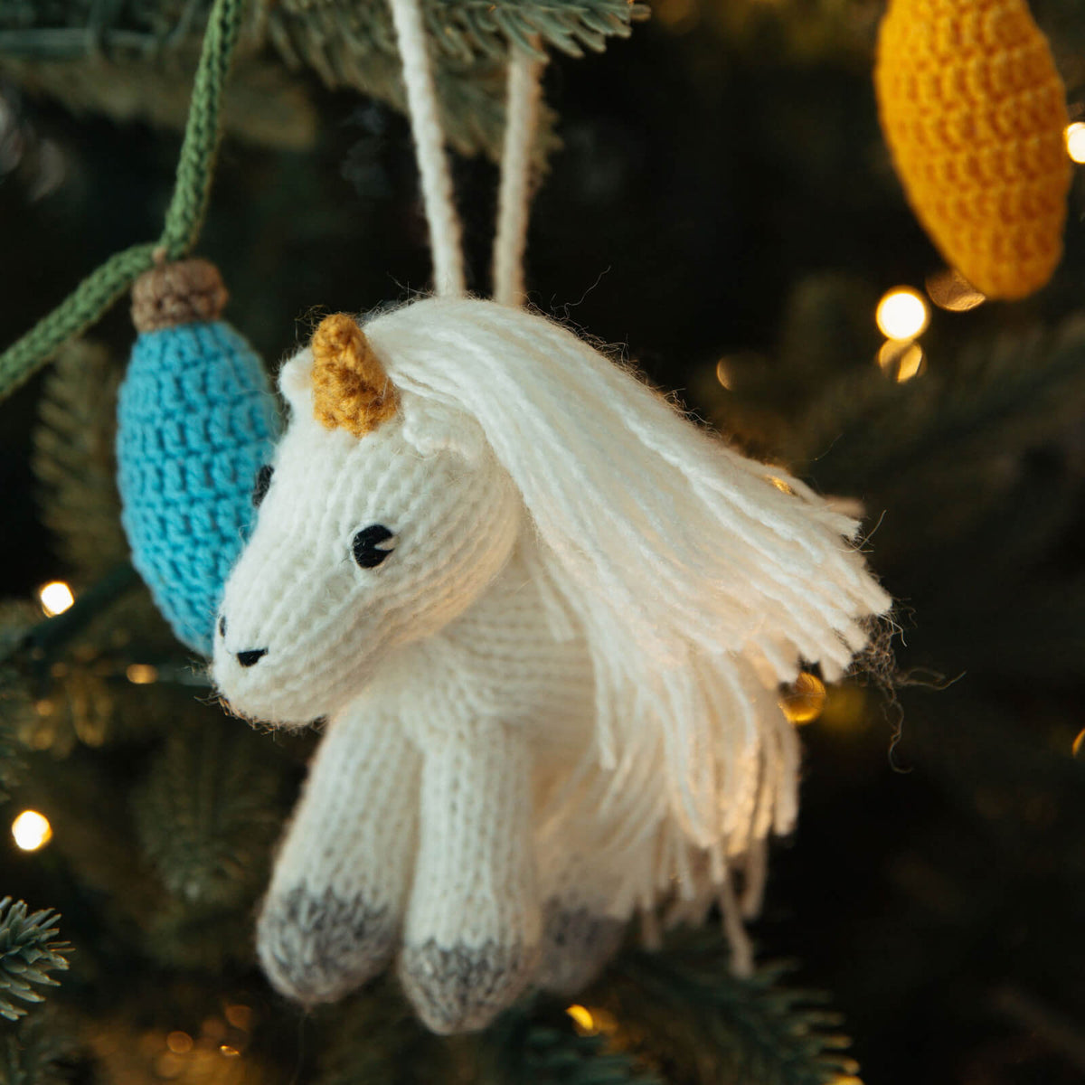 Knitted unicorn ornament hanging on a Christmas tree with blurred lights in the background