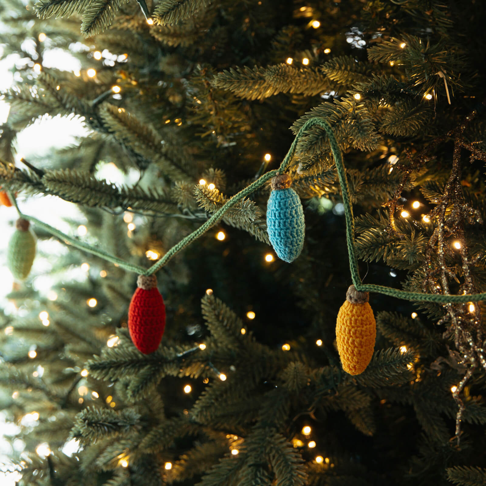 Decorative string lights with red, blue, and yellow crochet bulbs on a Christmas tree.