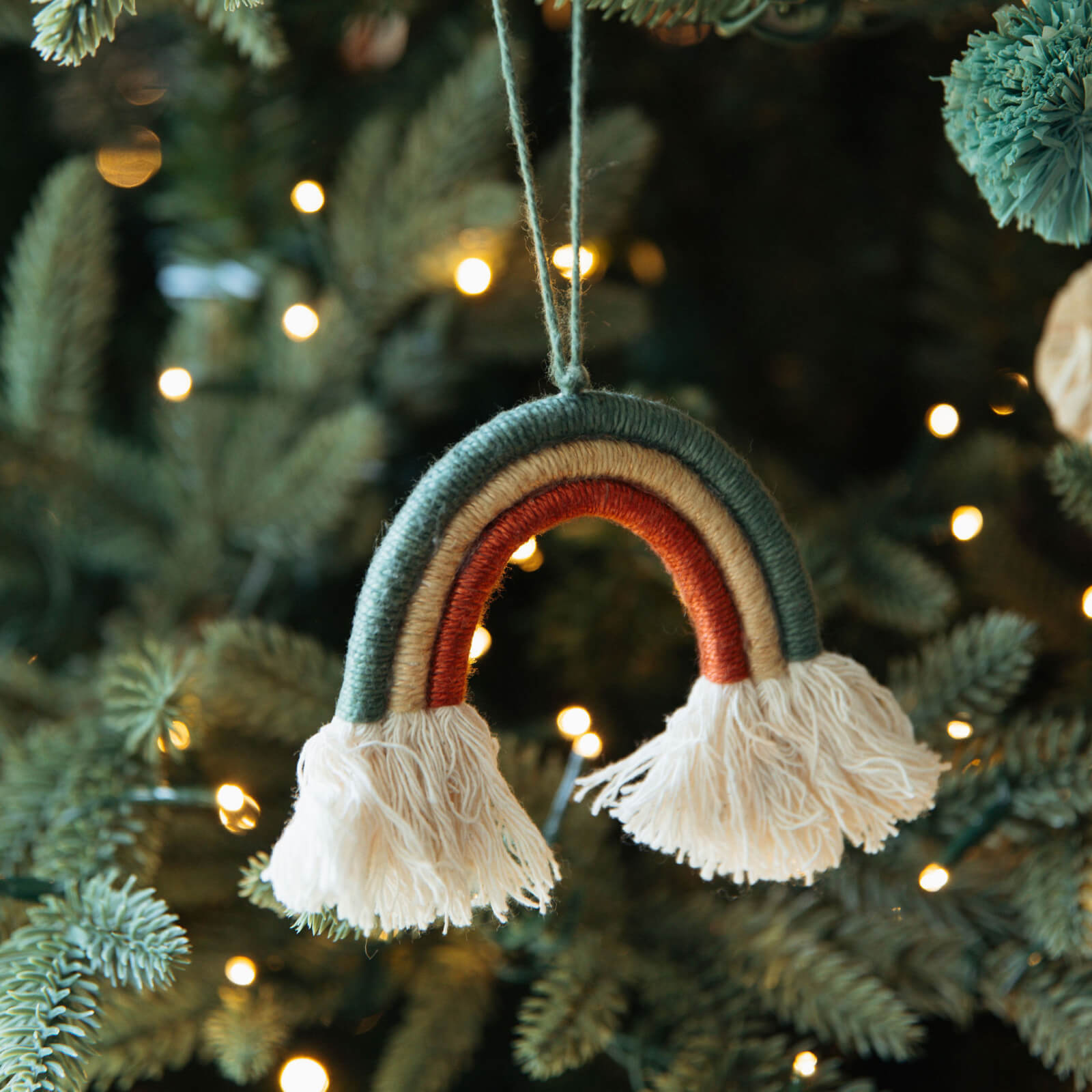 Decorative rainbow ornament with tassels hanging on a Christmas tree.