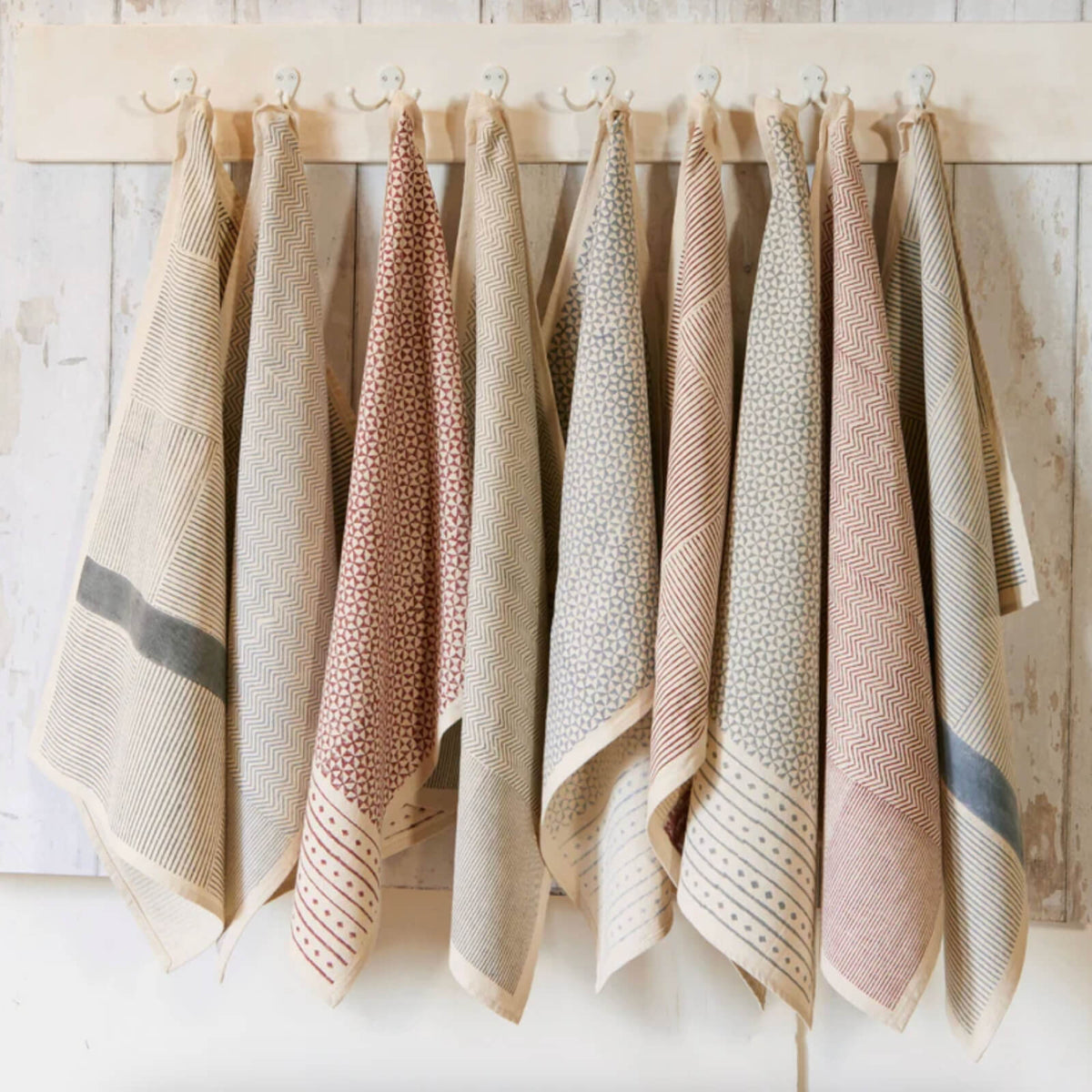 Set of patterned towels hanging on a wooden rack against a light wooden wall.