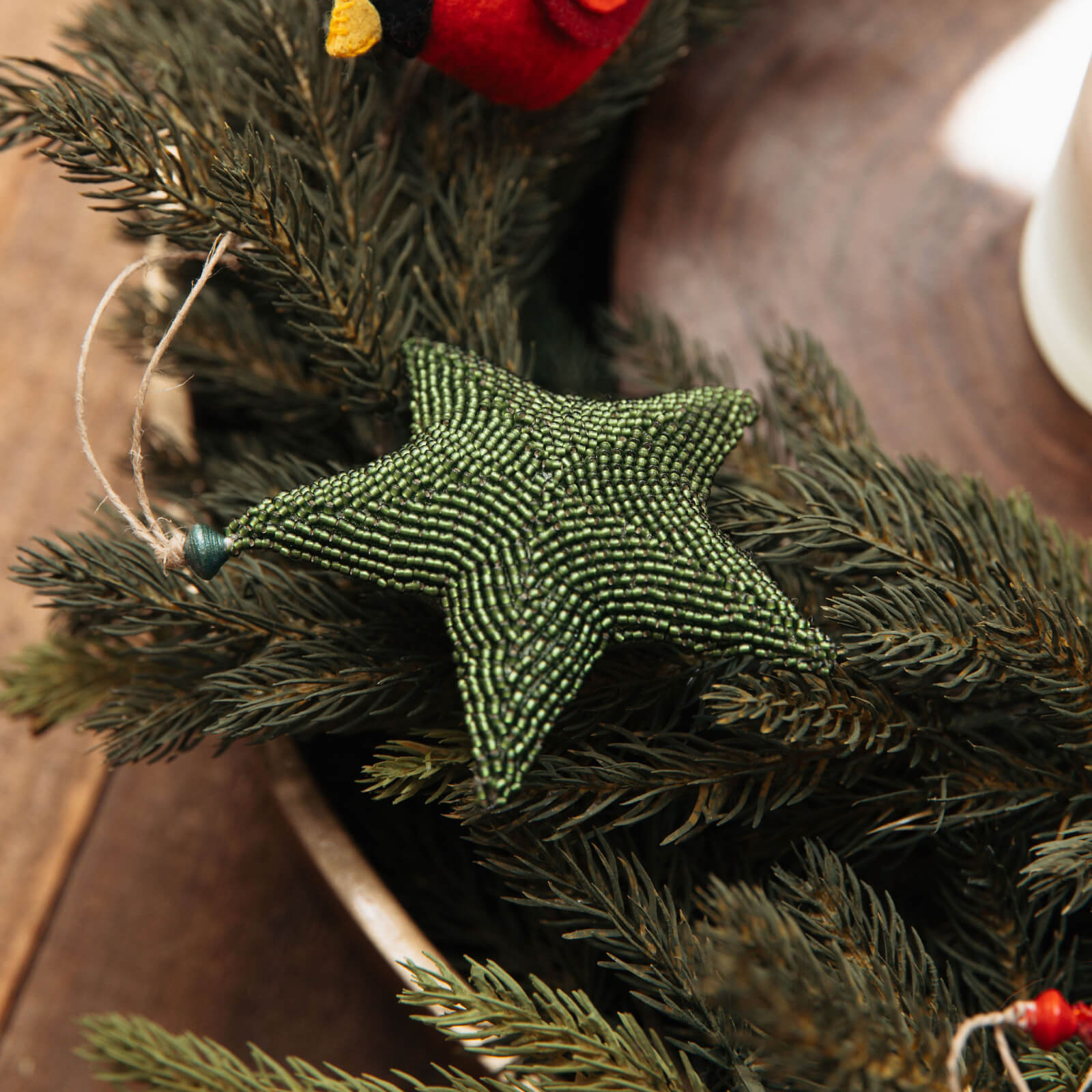 Green beaded star ornament on a Christmas wreath with red berries on a wooden surface.