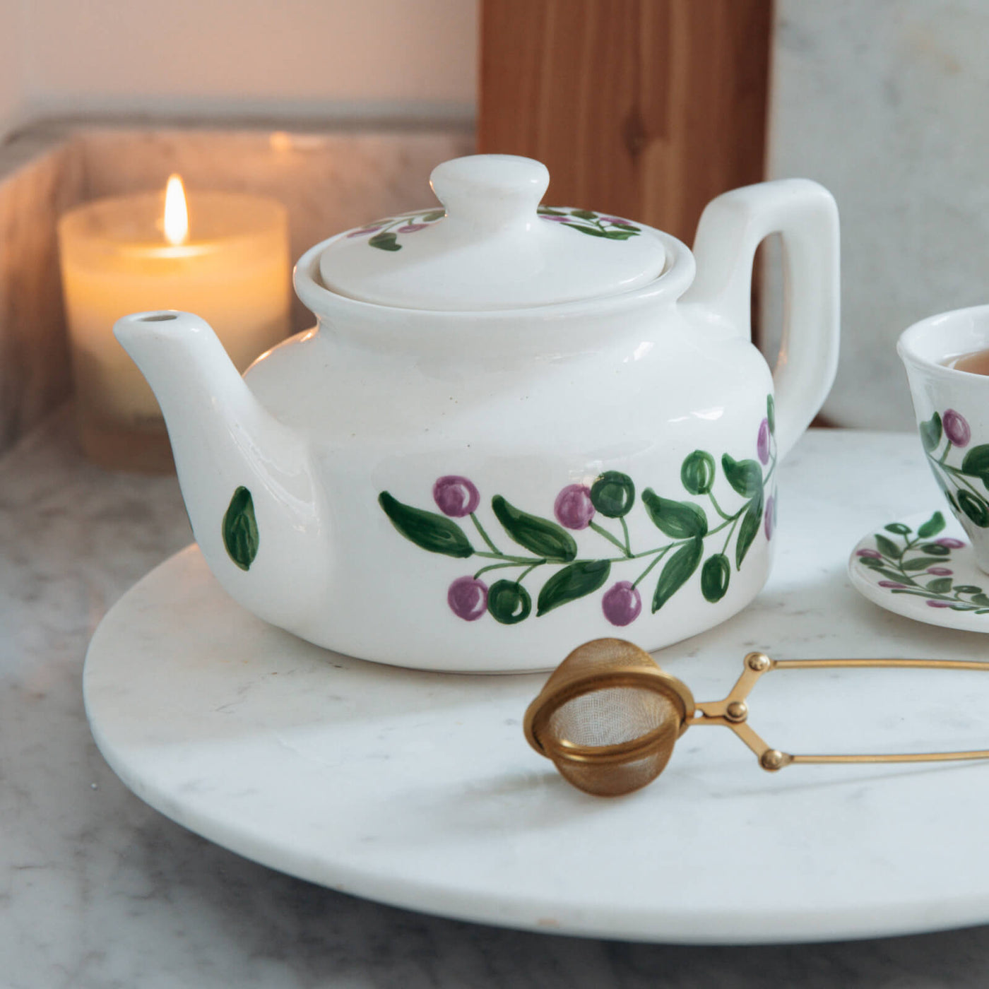 White teapot with floral design on a marble surface with a lit candle in the background