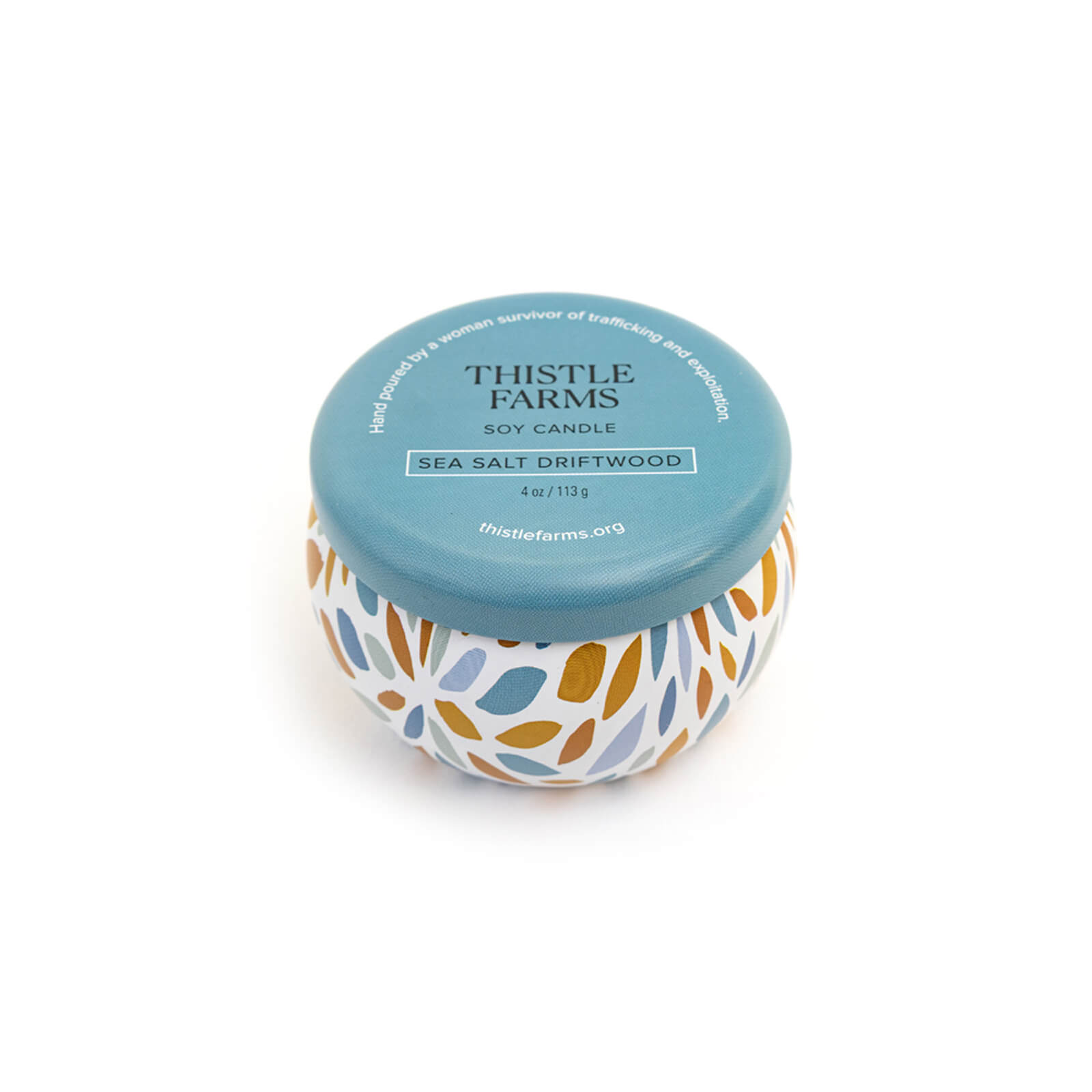 Candle jar with floral design and blue lid labeled 'Thistle Farms' on a white background