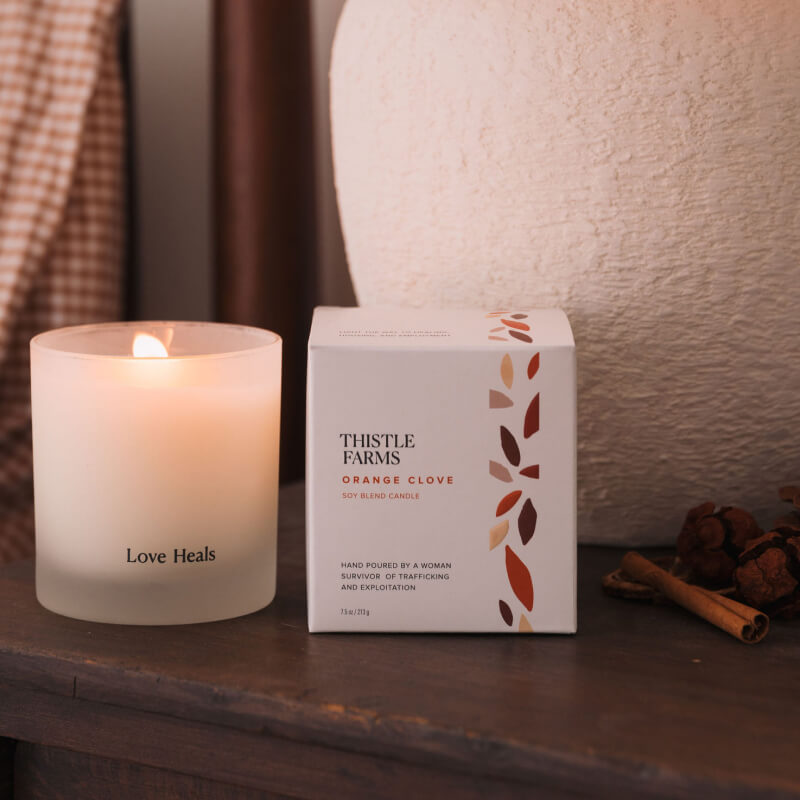 Frosted glass candle with box placed on wooden table against lamp. Candle is lit giving off a slight glow.