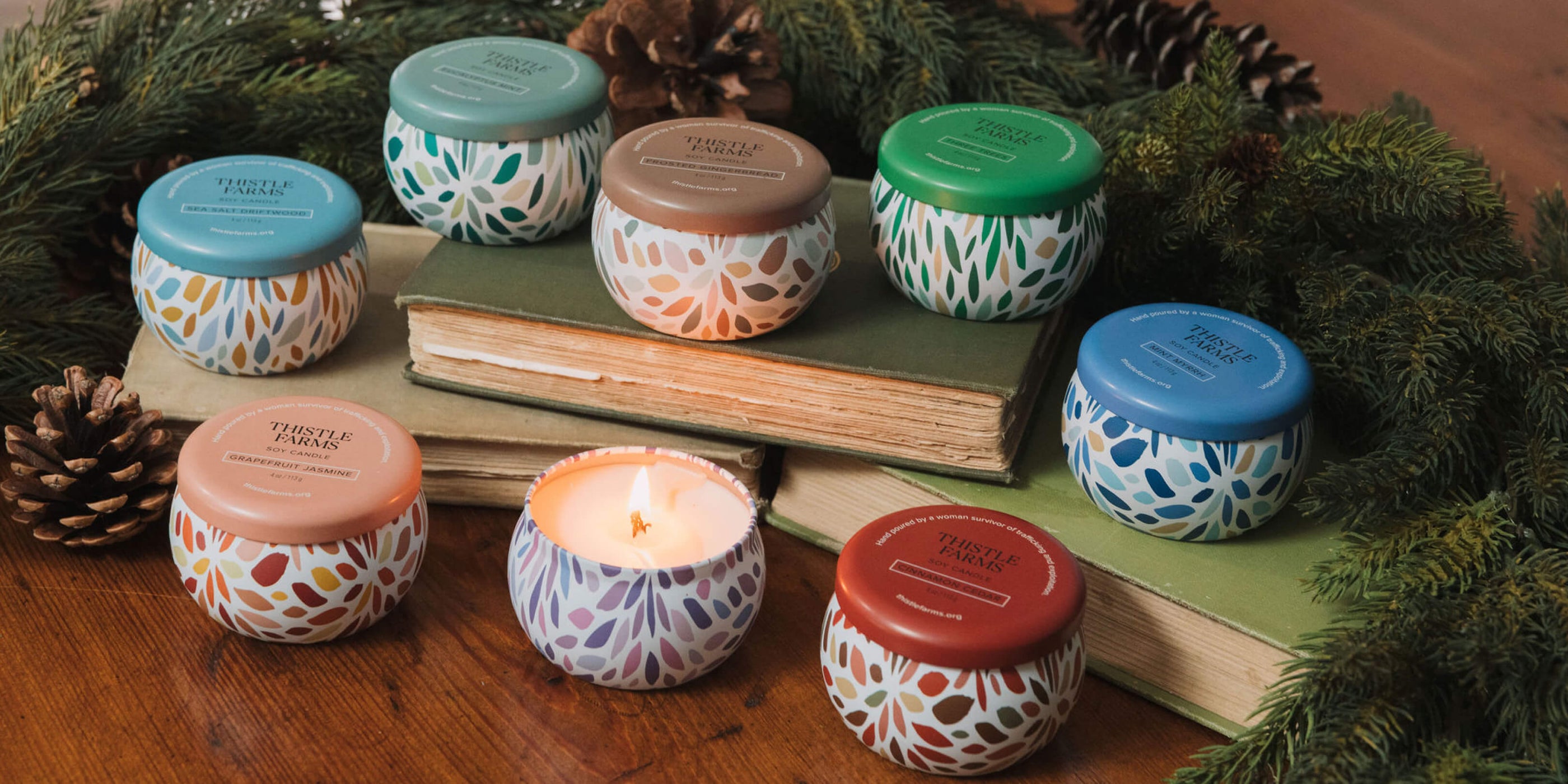 Set of small candles with decorative lids on a wooden surface with books and pine cones.
