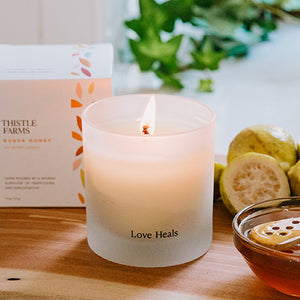 Guava Honey Candle with 'Love Heals' text on a wooden board next to guava fruit and honey.
