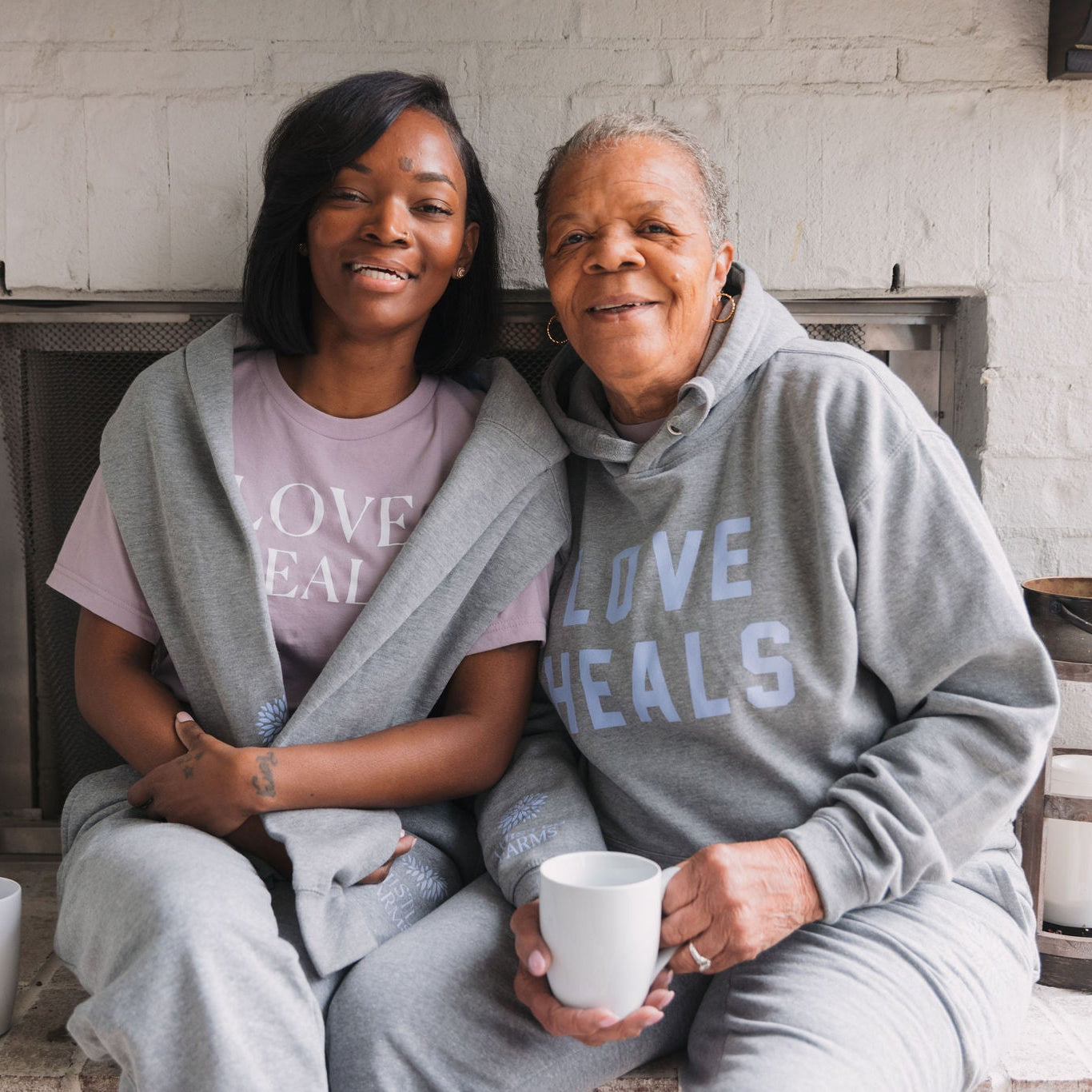 Two people wearing matching 'LOVE HEALS' outfits sitting together in a cozy indoor setting.