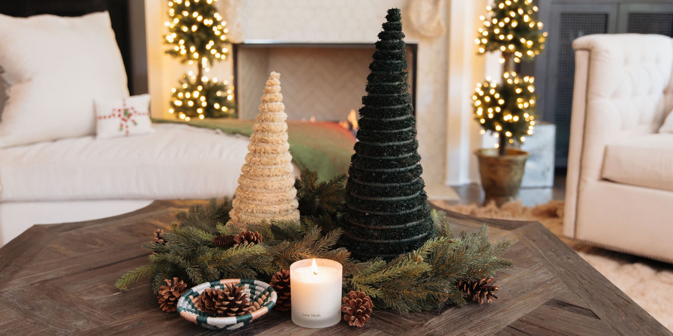 Decorative Christmas trees and candle on a coffee table in a living room with a fireplace.