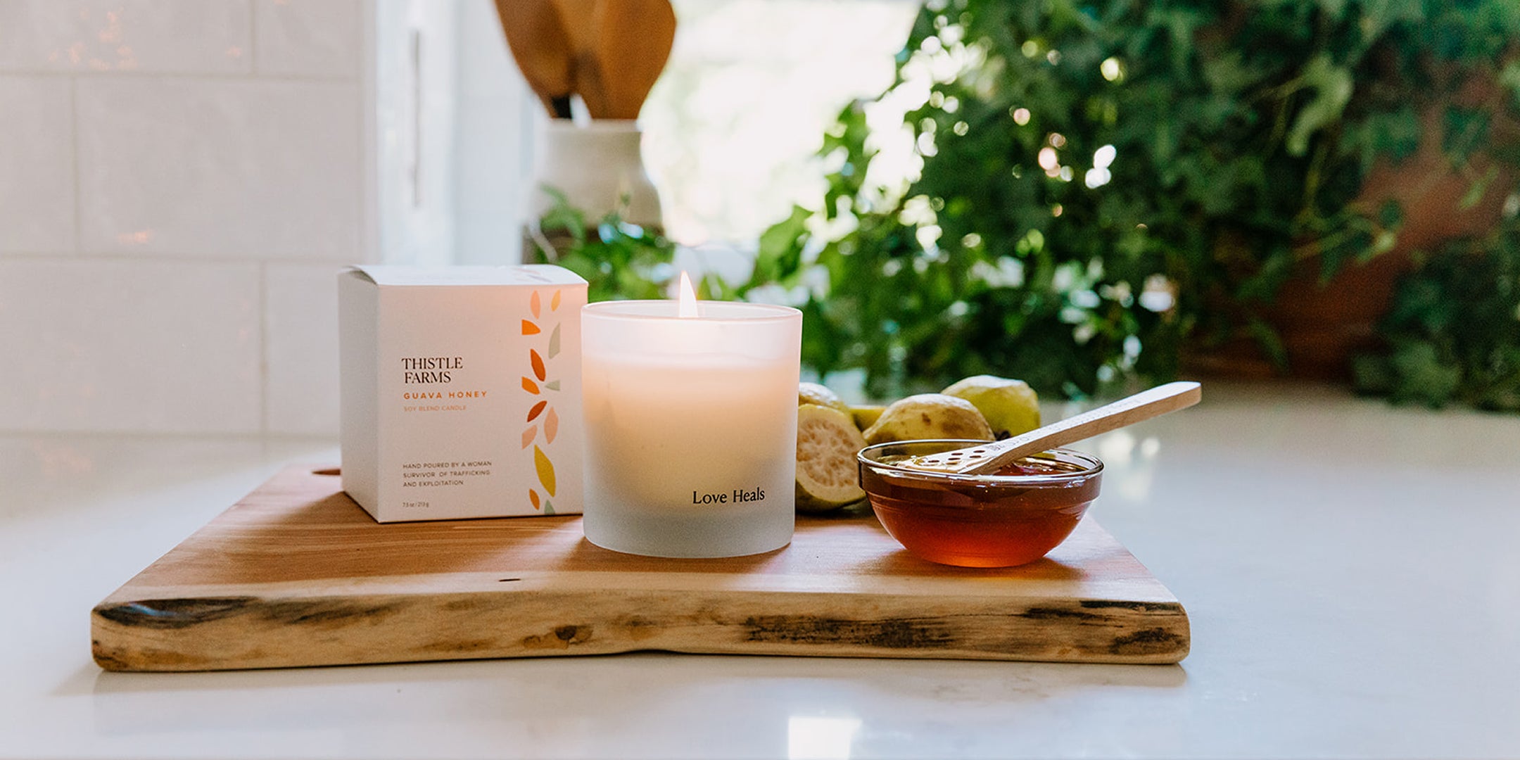 Guava Honey Candle with 'Love Heals' text on a wooden board next to guava fruit and honey.