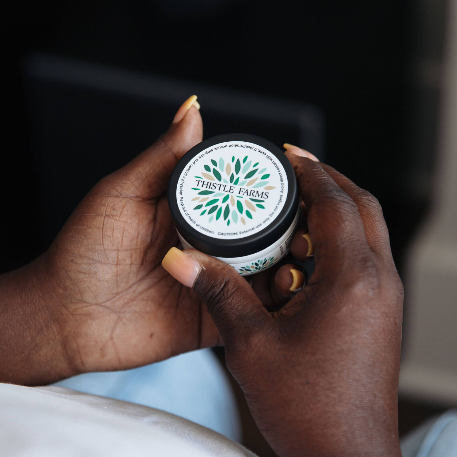 Two hands holding a jar of body butter with a blurred background