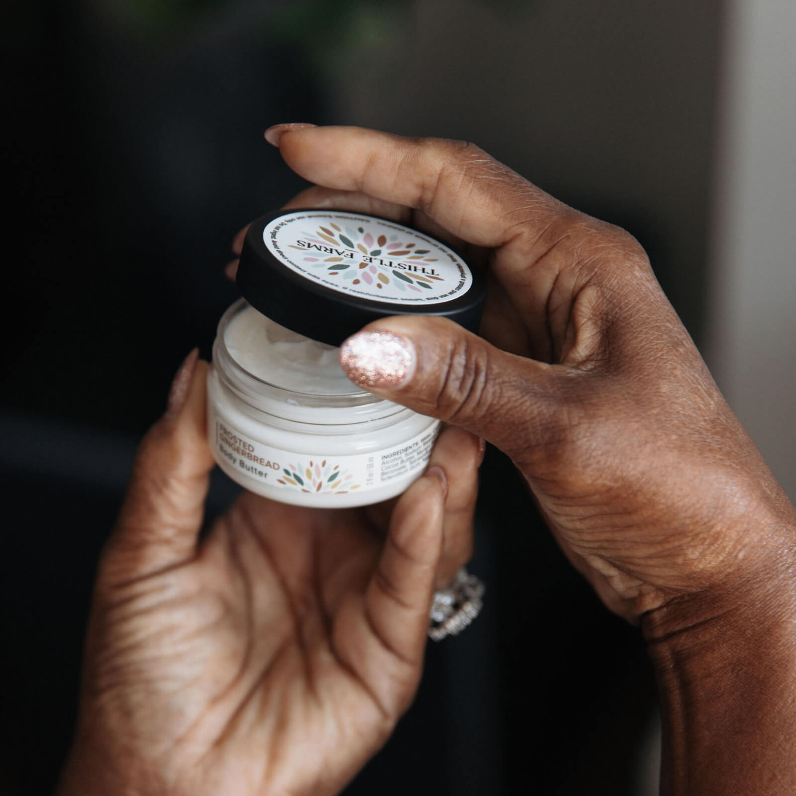 Two hands holding a jar of body butter with a blurred background