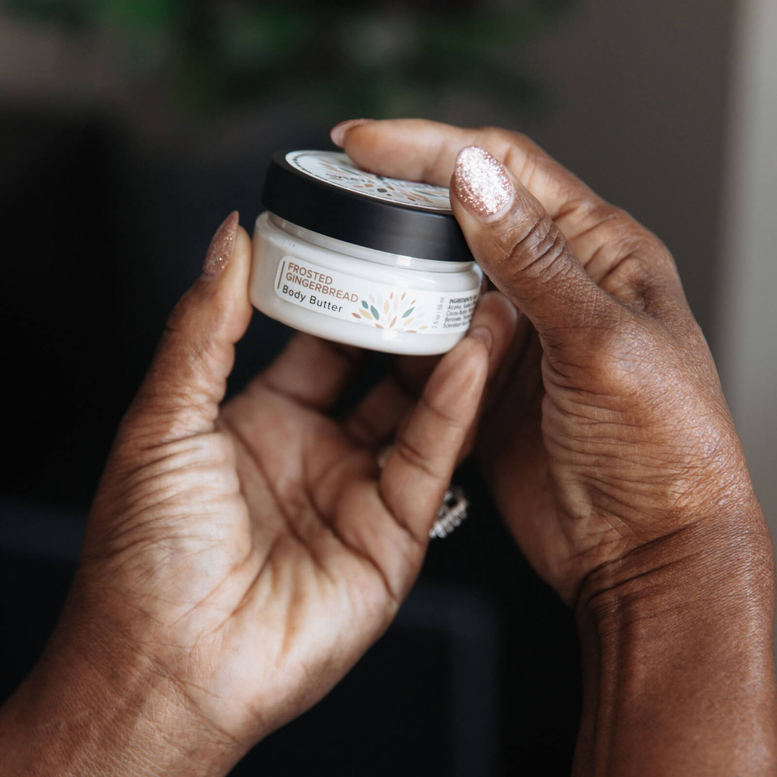 Two hands holding a jar of body butter with a blurred background