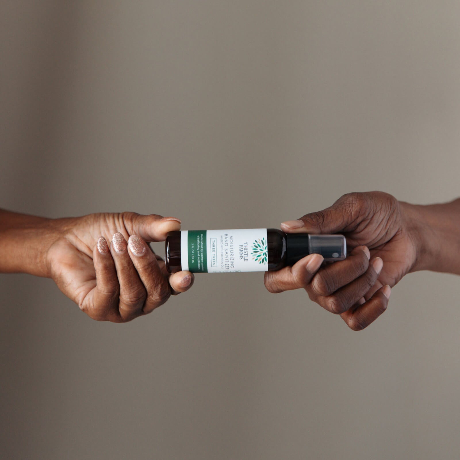 Two hands holding a hand sanitizer bottle with a green label against a neutral background