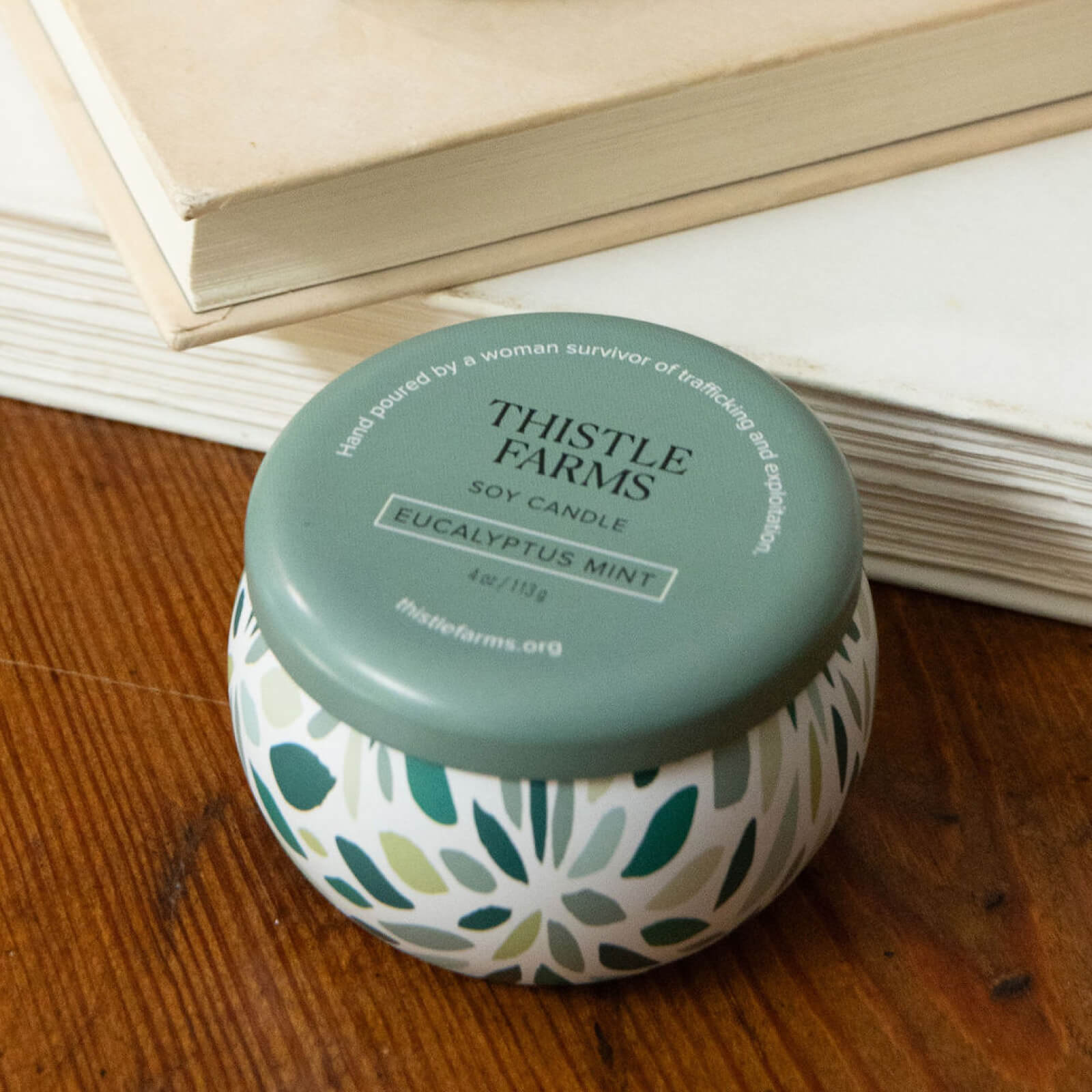 Thistle Farms soy candle with a green lid on a wooden surface