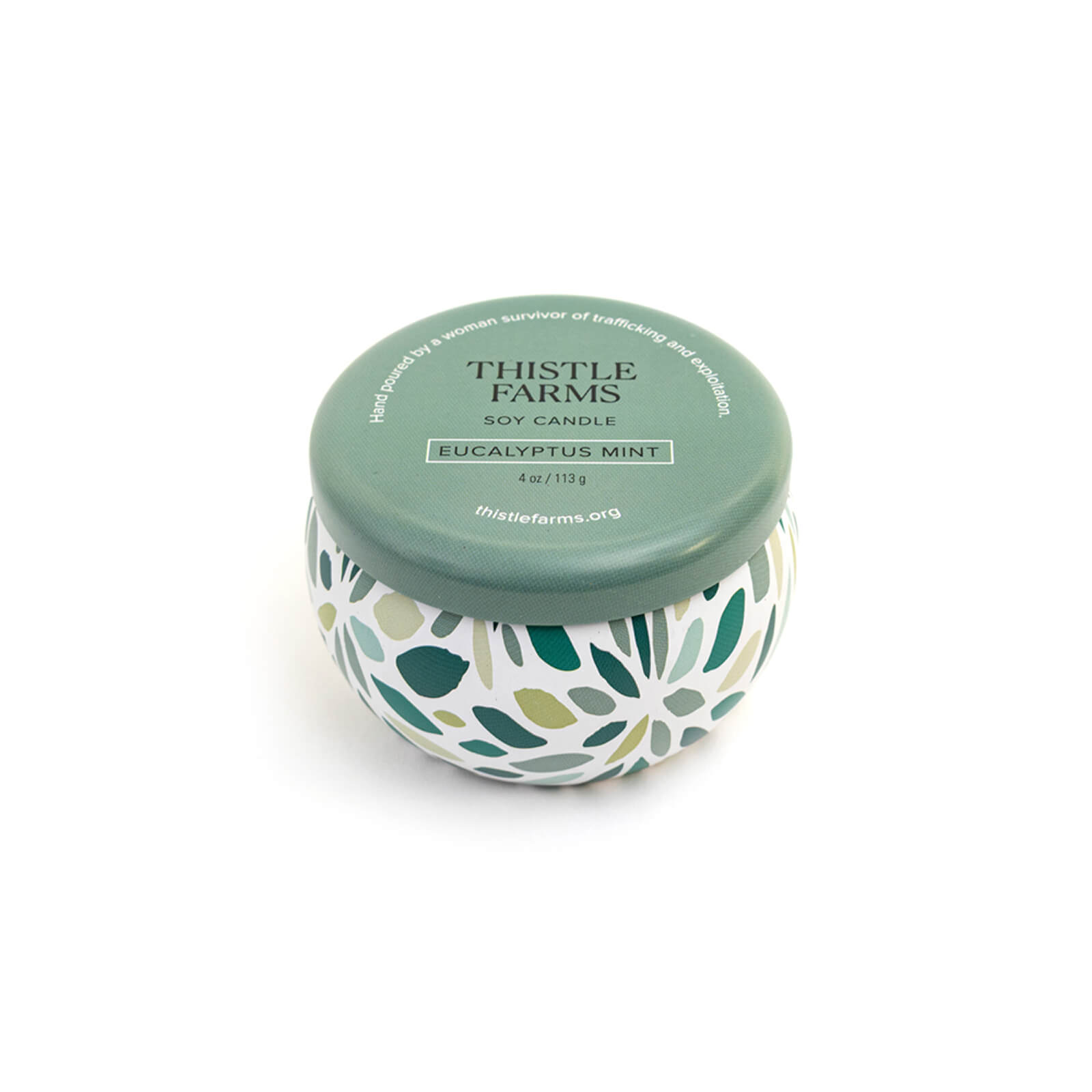 Thistle Farms soy candle with green lid and leaf patterned base on a white background