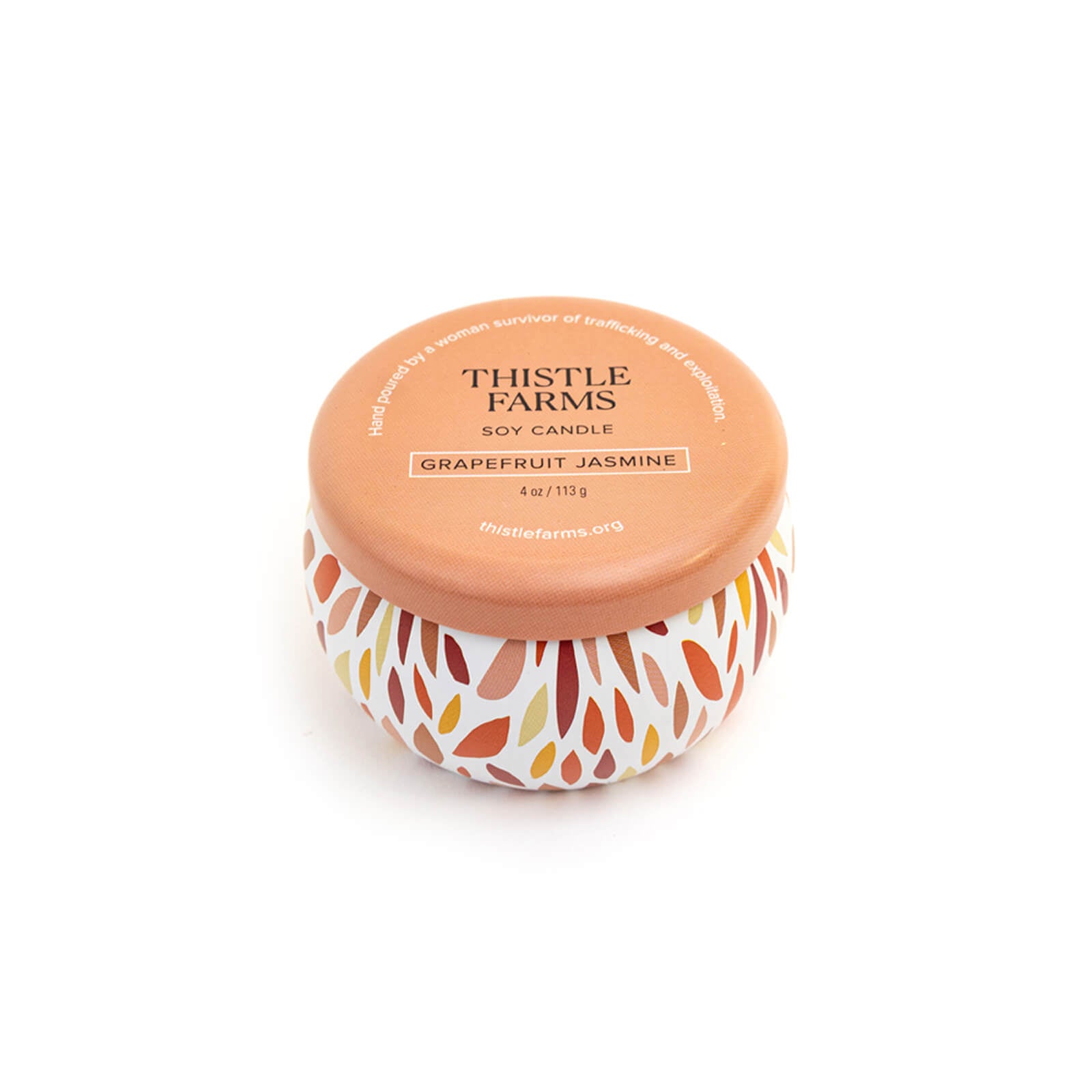 Thistle Farms soy candle with a leaf patterned base and orange lid on a white background