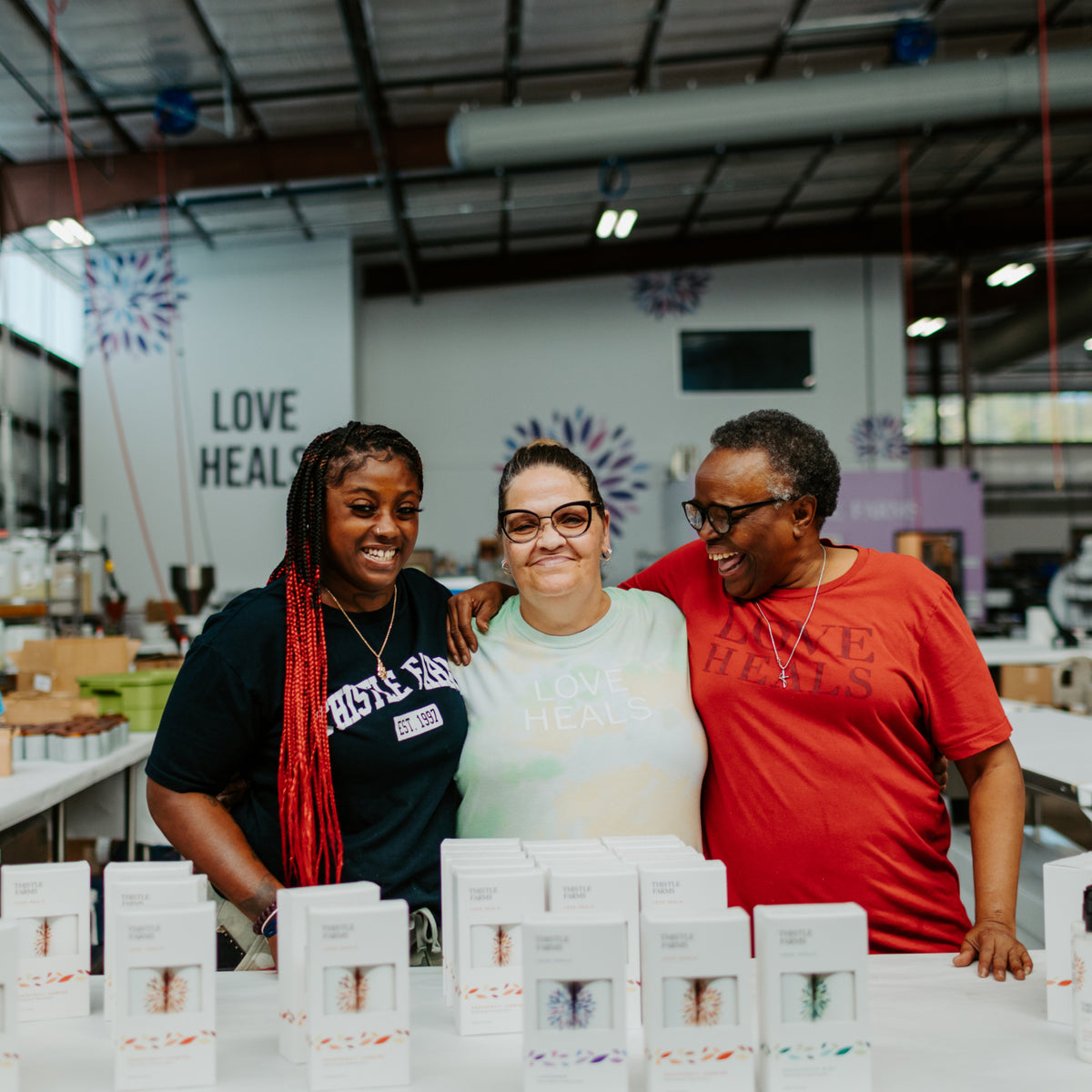 Three women standing together in a warehouse setting with boxes in front of them.