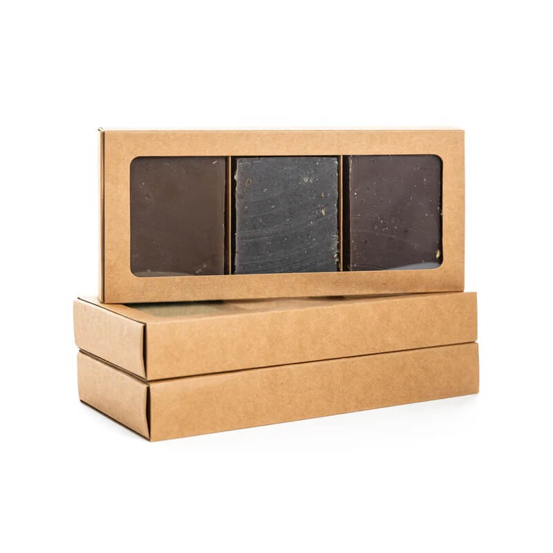 Three dark-colored soap bars in a cardboard box with a clear window on a white background