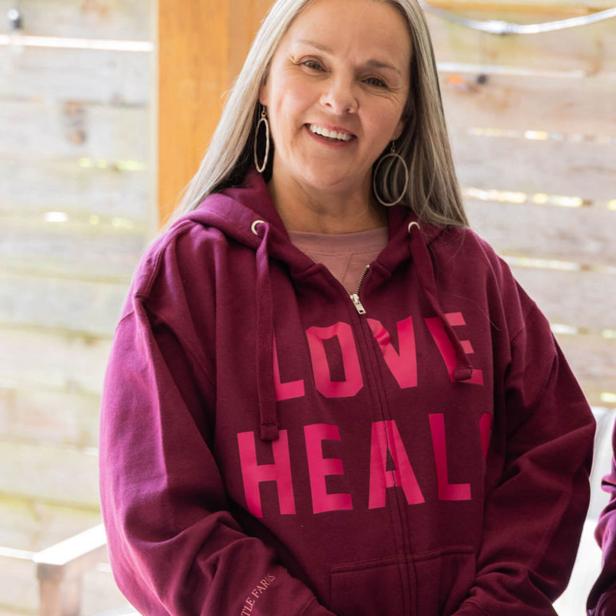 Woman wearing a maroon hoodie with 'LOVE HEALS' text, standing indoors.