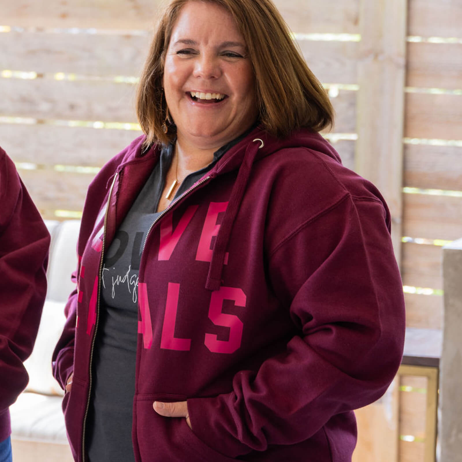 Person wearing a maroon hoodie with pink text indoors