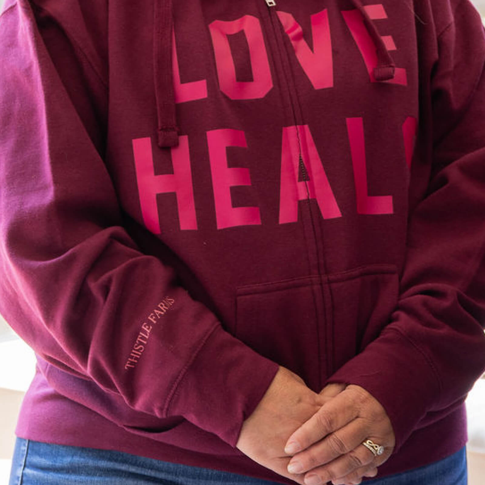 Maroon hoodie with pink text 'LOVE HEALS' worn by a person.