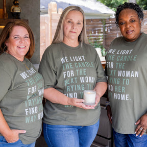 Three women wearing matching green t-shirts with 'WE LIGHT THE CANDLE FOR THE NEXT WOMAN TRYING TO FIND THEIR WAY HOME.'