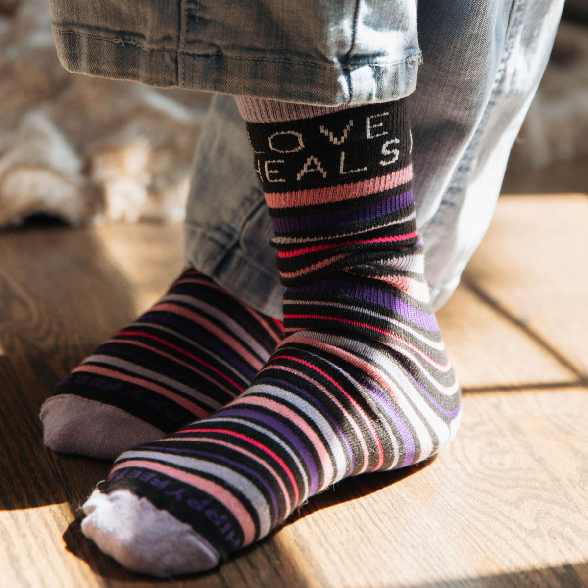 Striped socks with 'LOVE HEALS' text worn by a person on a wooden floor.