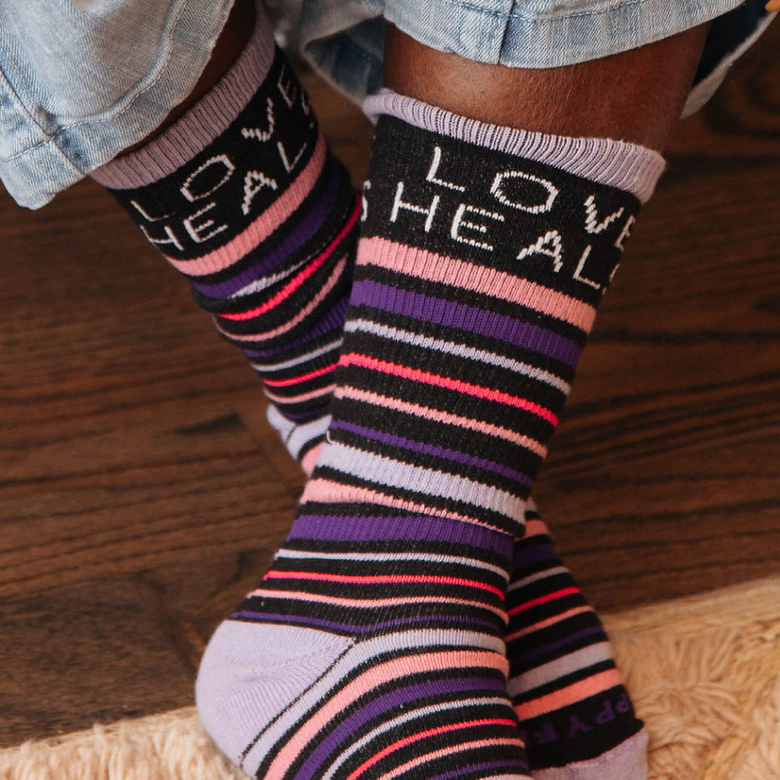 Colorful Love Heals Stripe Socks with 'LOVE HEALS' text worn by a person on a wooden floor.
