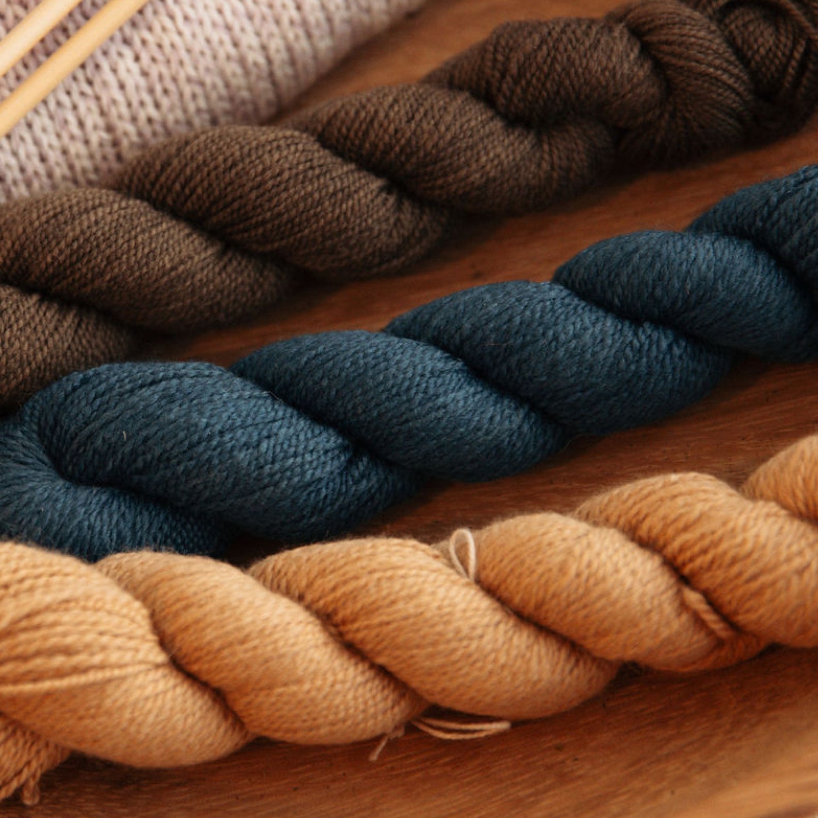 Three skeins of yarn in brown, blue, and beige on a wooden surface