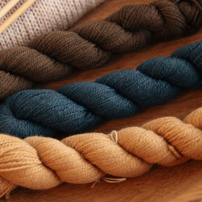 Three skeins of yarn in brown, blue, and beige on a wooden surface