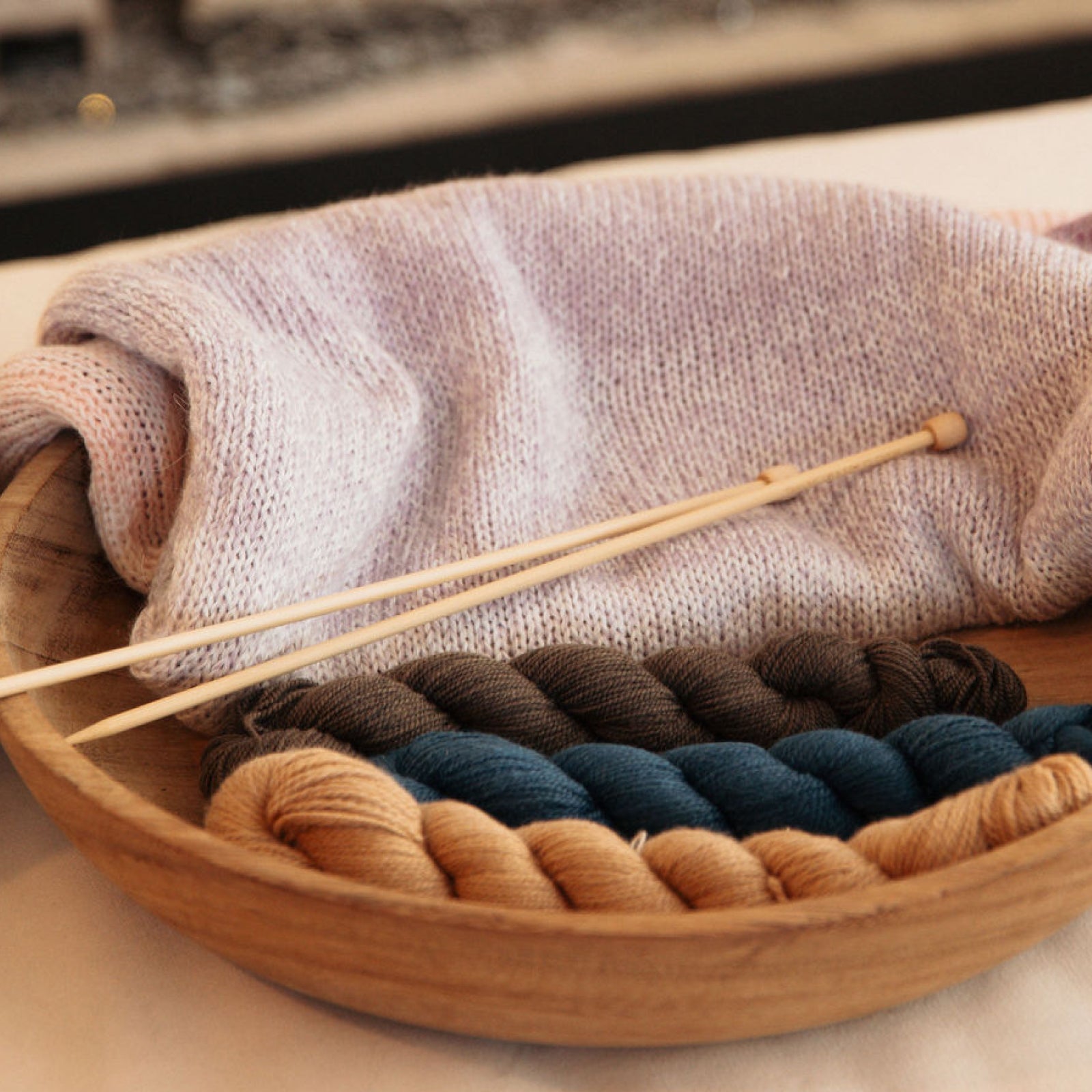 Wooden bowl with yarn and knitting needles on a textured surface