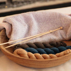 Wooden bowl with yarn and knitting needles on a textured surface