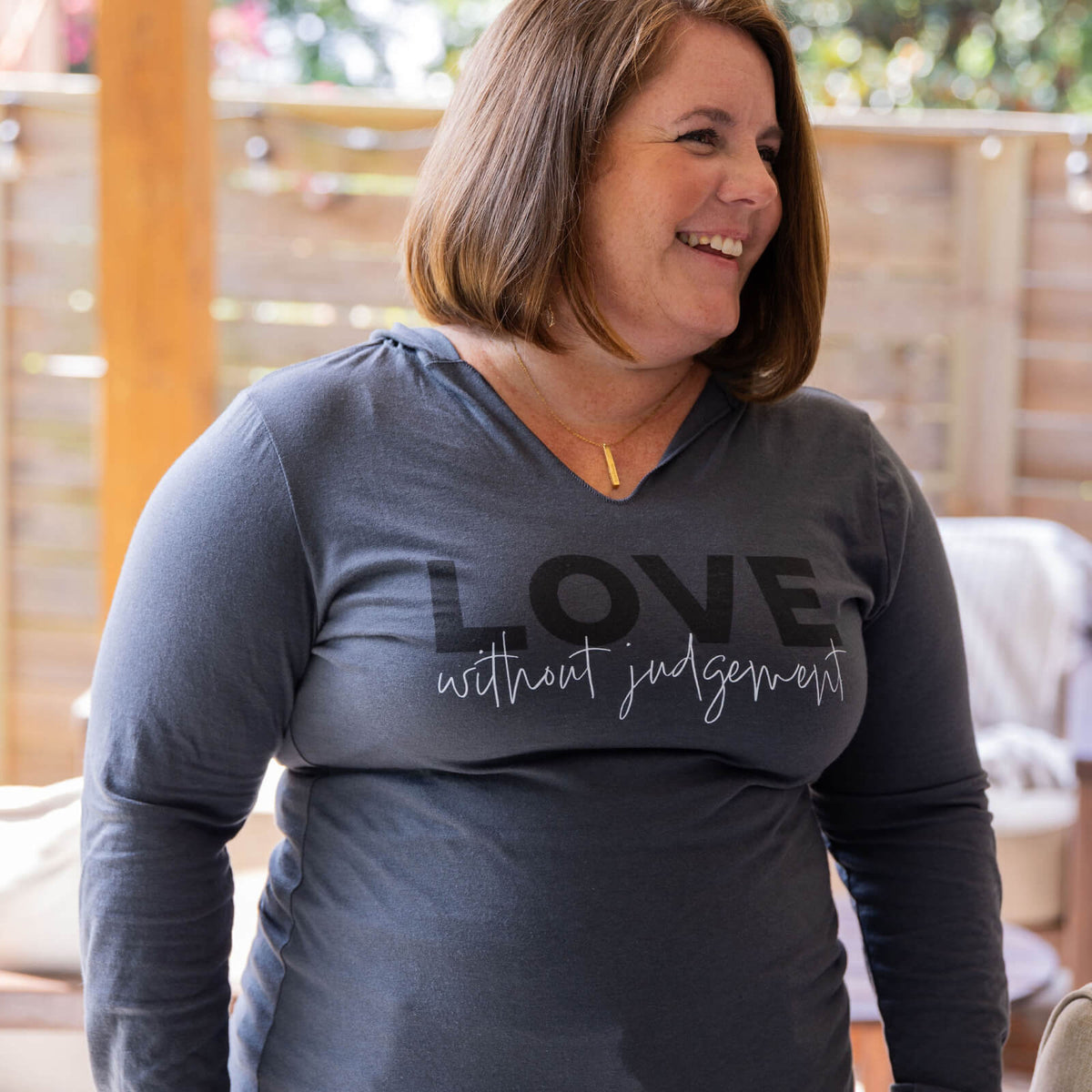 Woman wearing a gray long-sleeve shirt with 'LOVE without judgement' text outdoors.